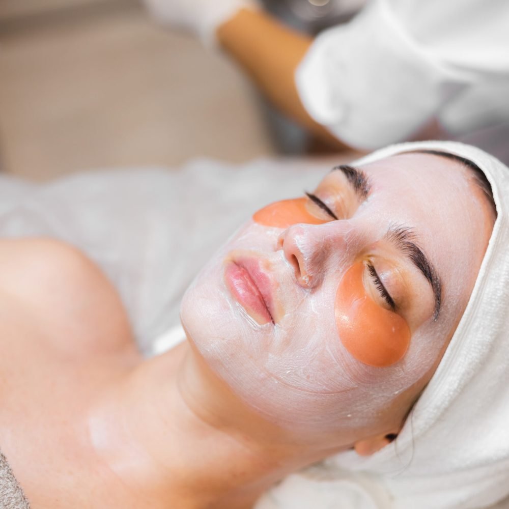 A young girl in a beauty salon in a cosmetology room lies on a bed relaxes with a mask on her face and patches under her eyes
